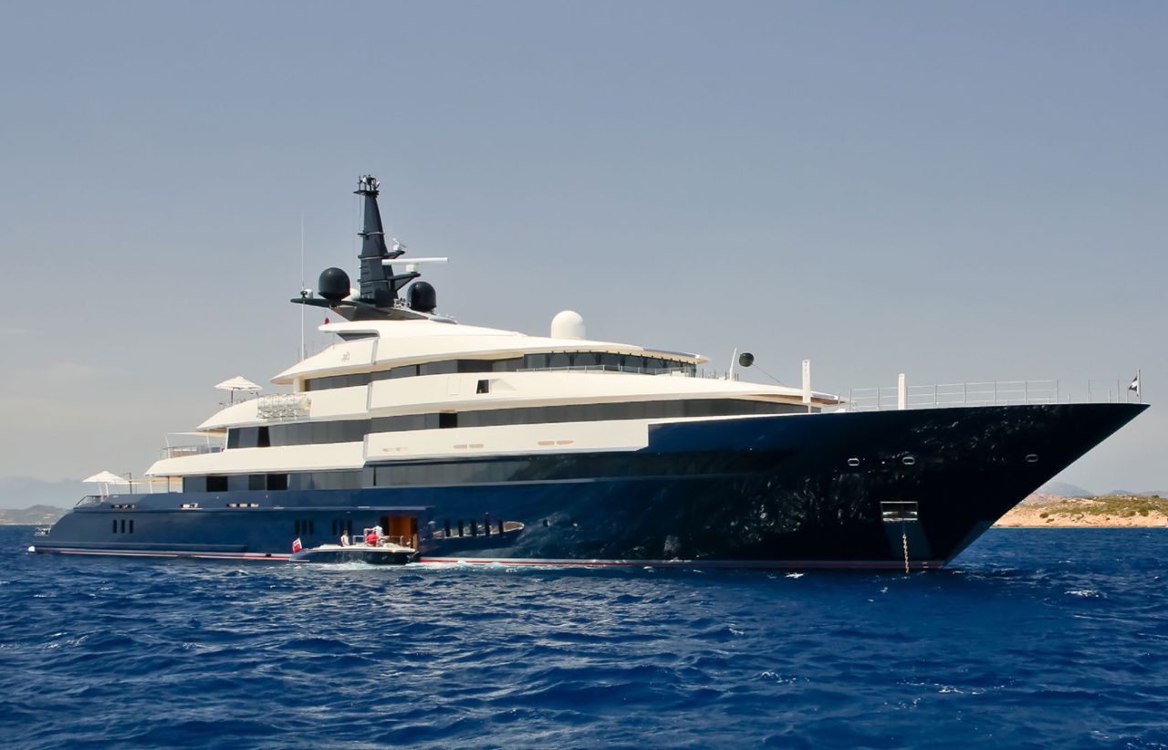 Large luxury yacht with dark blue hull and white superstructure on clear blue water.