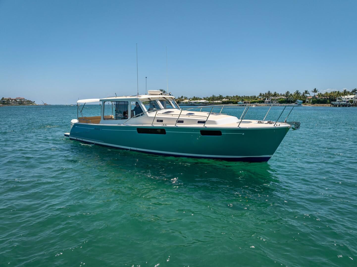 Teal motorboat with white cabin cruising on clear turquoise water under a blue sky.
