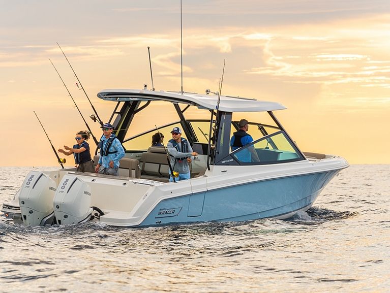 Blue and white fishing boat with four people fishing on calm water at sunset.