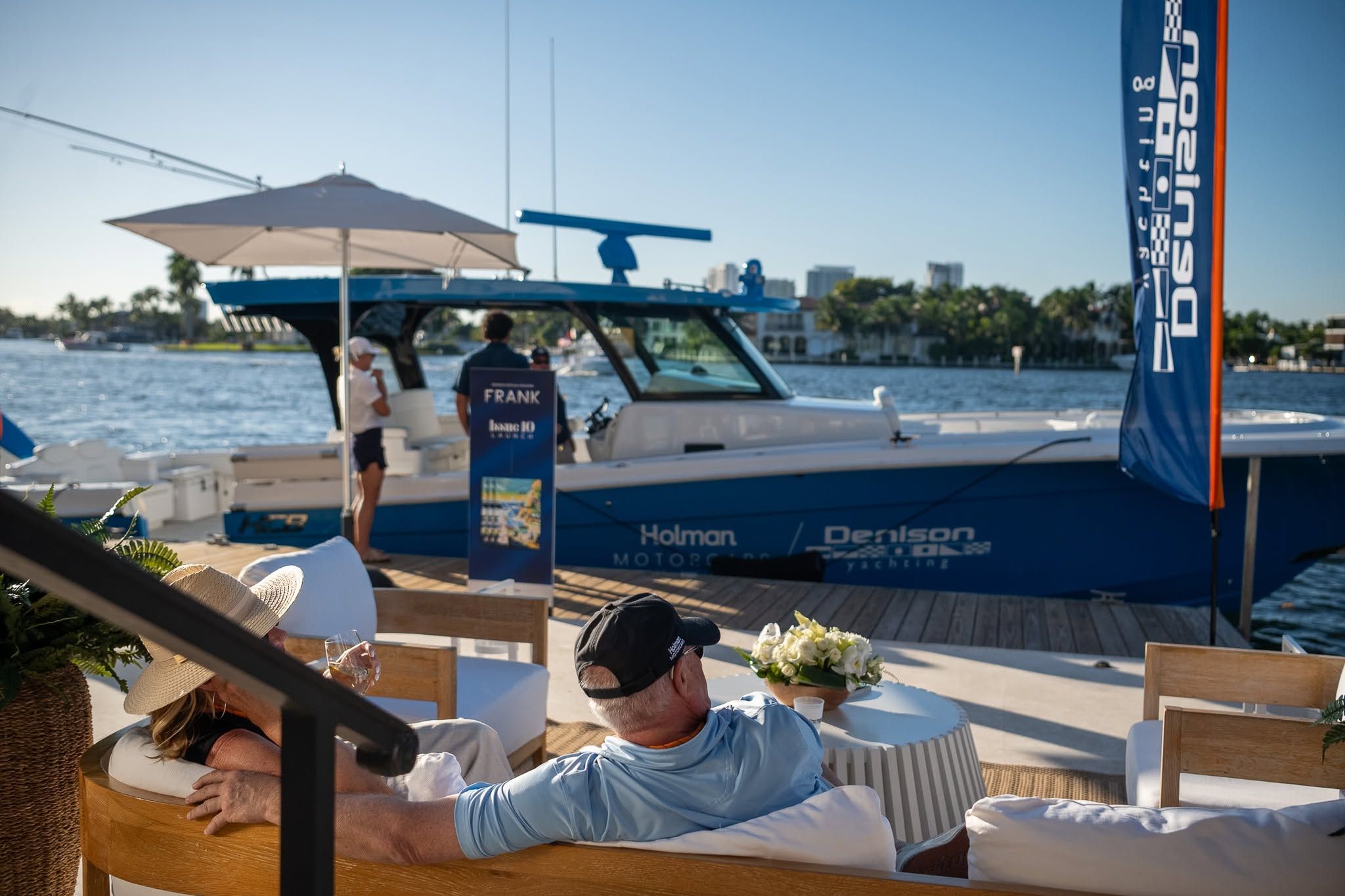 Blue recreational yacht docked at a marina with people relaxing on shore.
