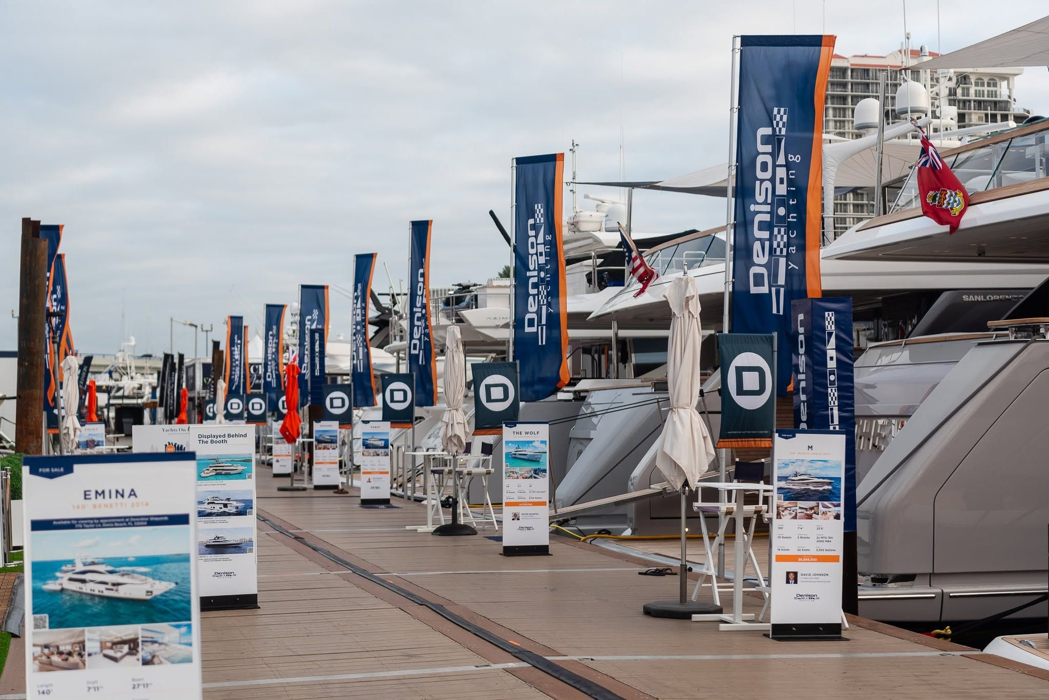 A row of Denison Yachting flags and promotional stands line a pier leading to luxury yachts.