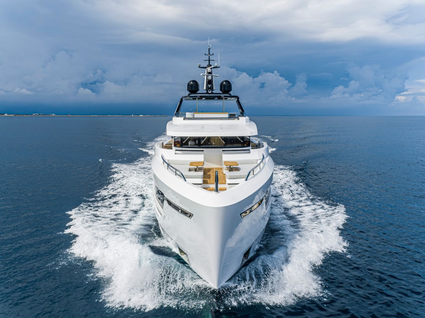 Large white luxury yacht cruises through blue ocean water, creating a foamy wake.