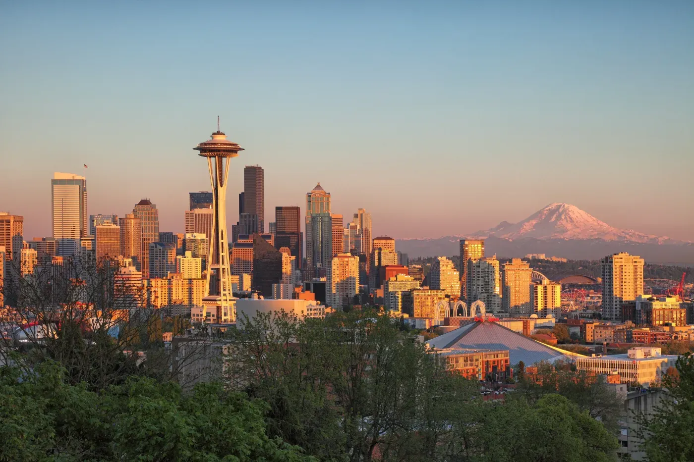 Golden hour light bathes Seattle's skyline, Space Needle, and distant Mount Rainier.