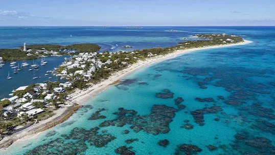 Aerial view of a tropical island, sandy beach, turquoise ocean, harbor, and lighthouse.