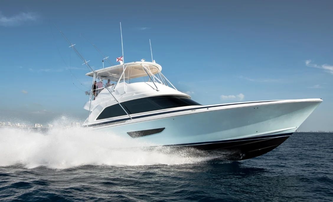 A sleek white sportfishing yacht speeds across blue ocean waters, creating a large white wake.