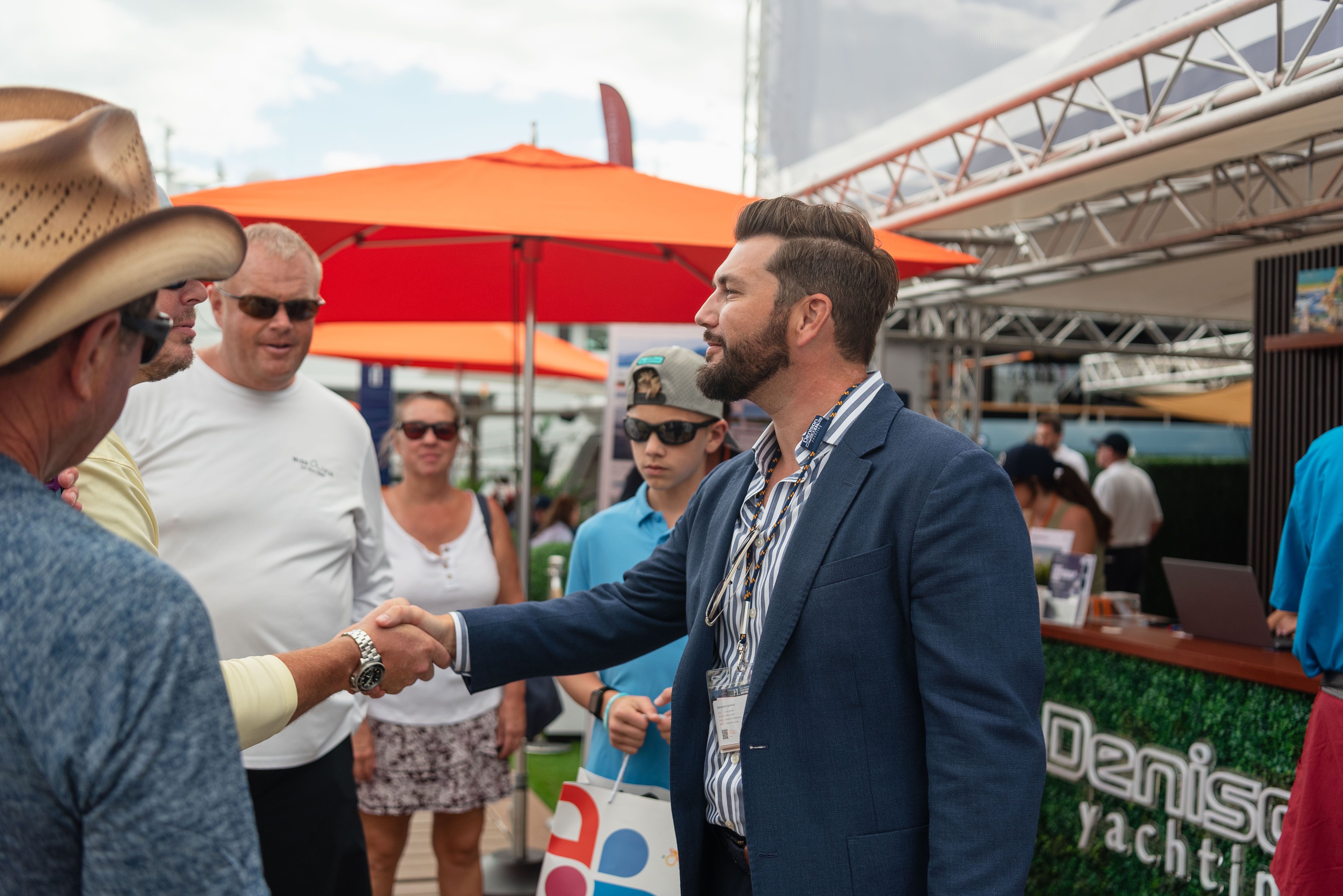 Two men shake hands at an outdoor event near a Denison Yachting booth.
