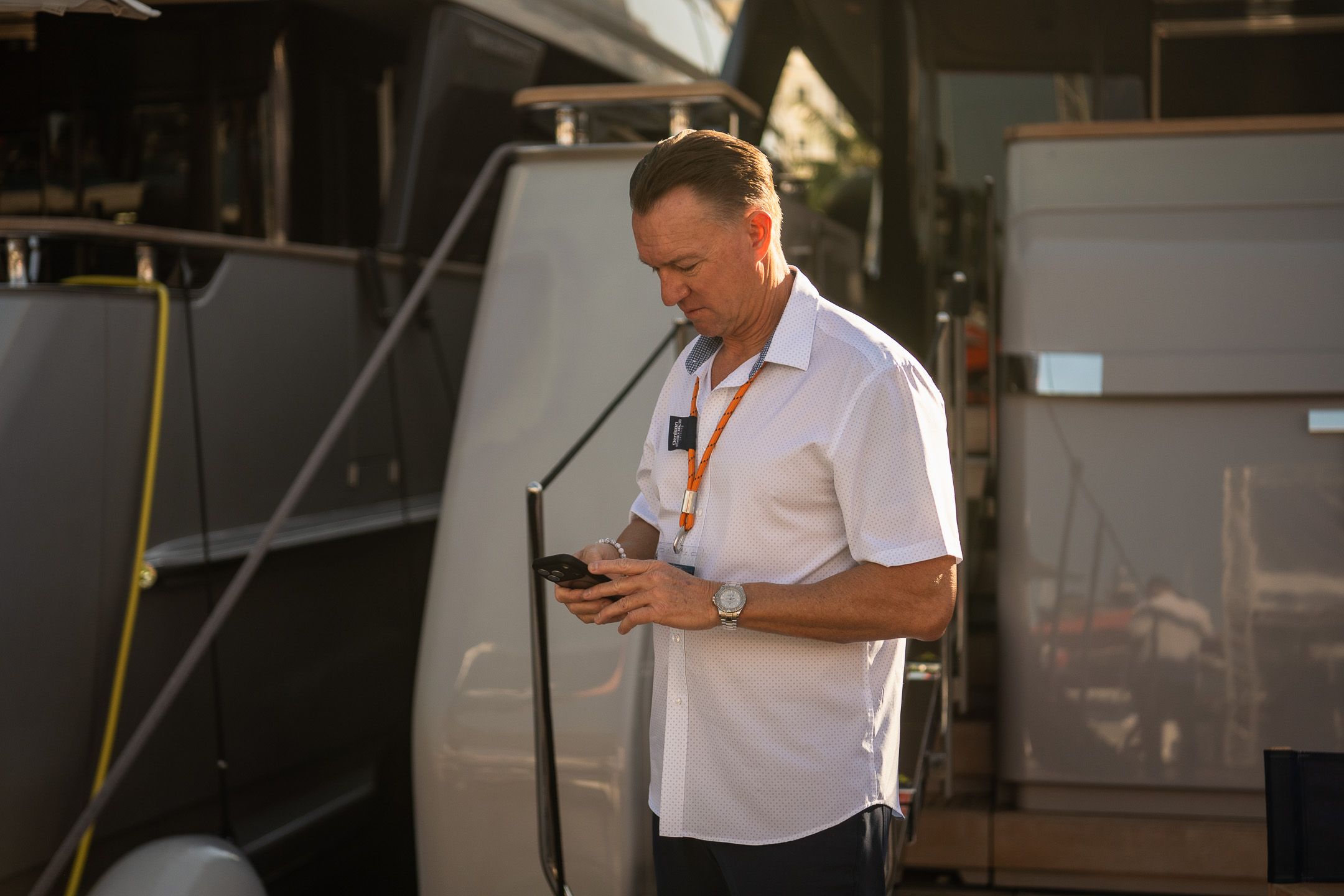 Man in white shirt looking at his smartphone next to a large grey structure.