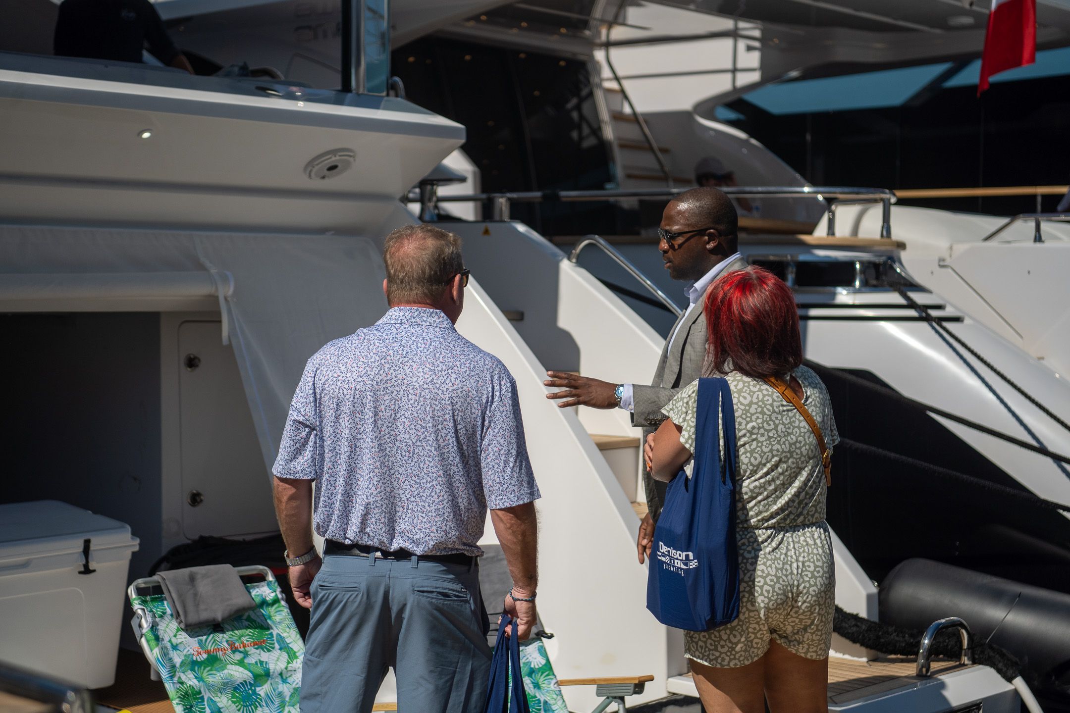 A man gestures while speaking with two people near a large white yacht.