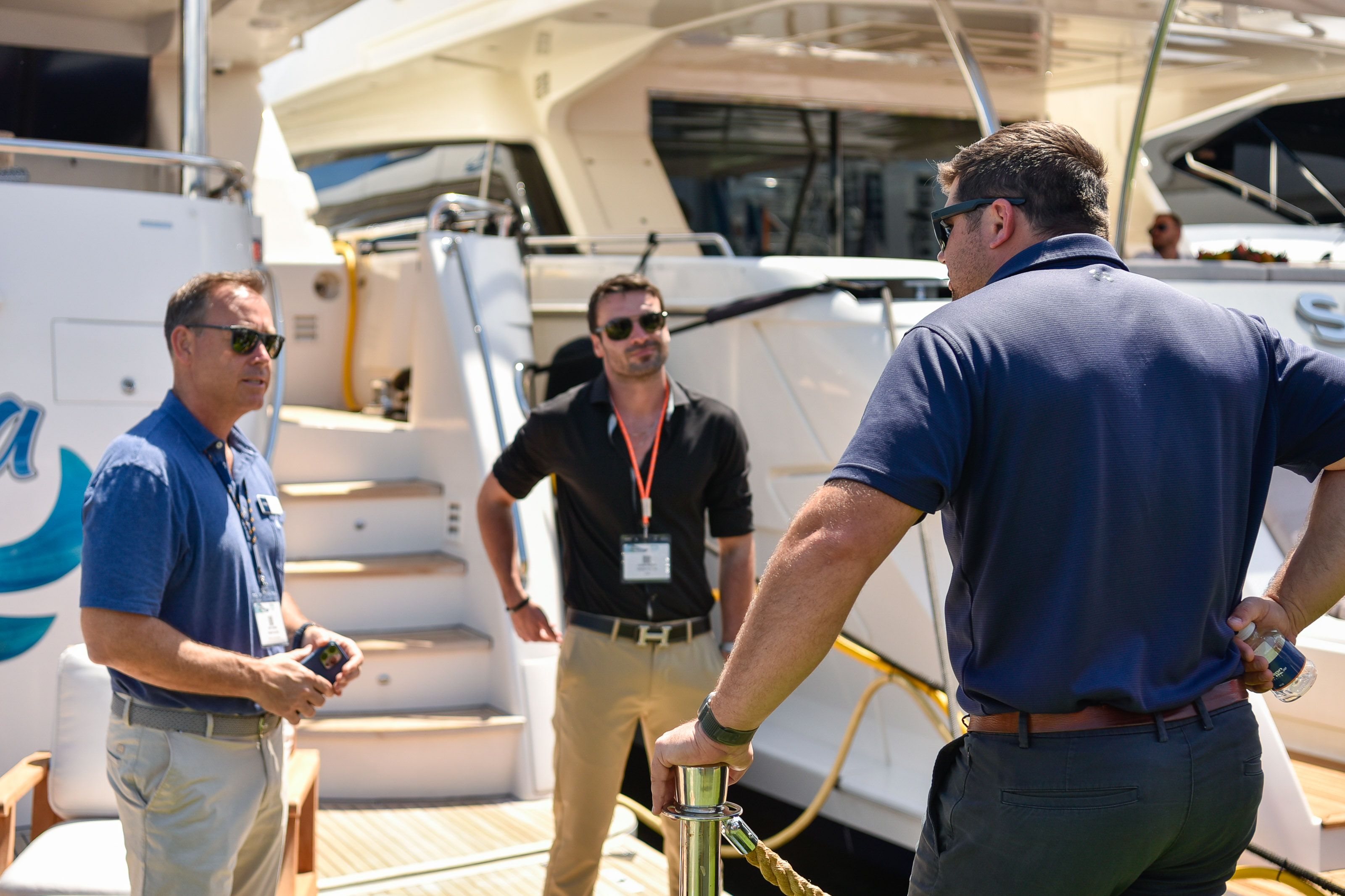 Three men in polo shirts conversing on the deck of a yacht under sunny skies.