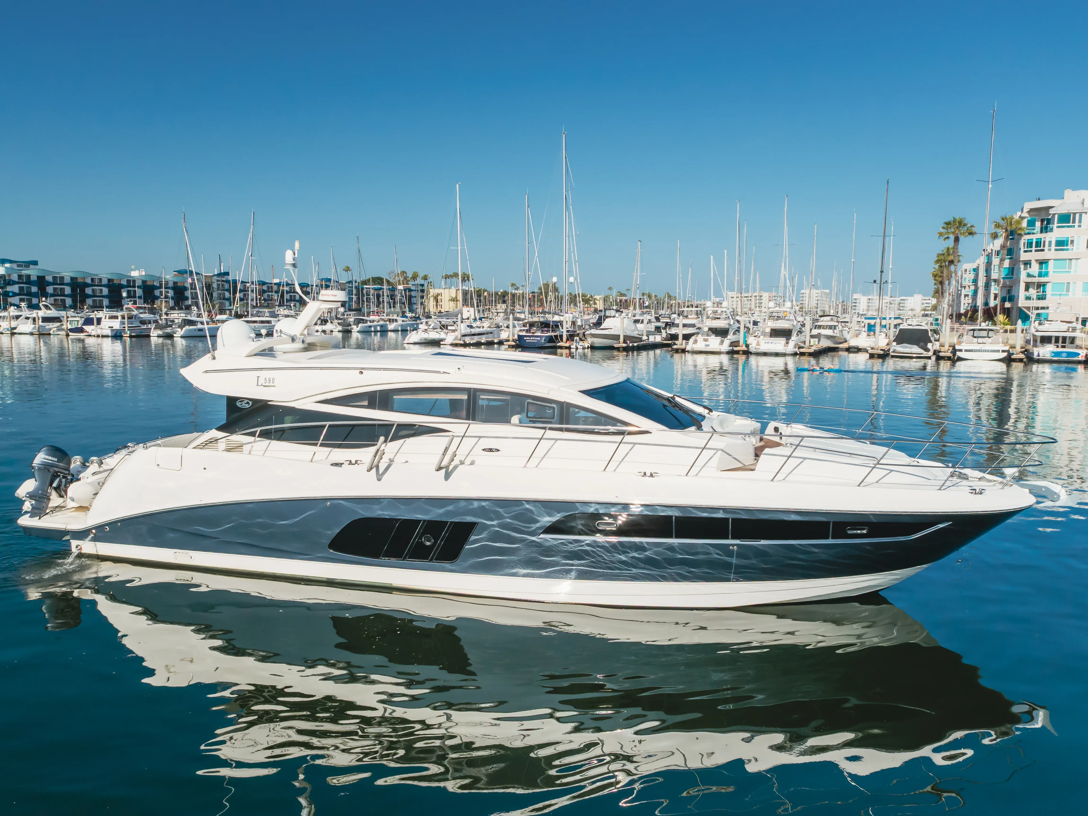 A sleek white and blue luxury yacht docked in a sunny marina with other boats.