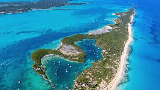 Aerial view of a narrow, green island with turquoise ocean, boats in calm inlets.