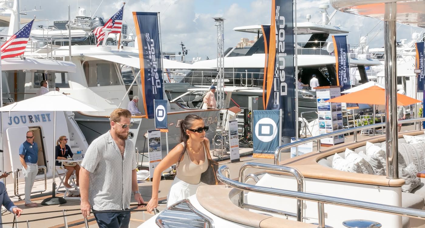 Man and woman walk past luxury yachts with 'OCEANCO' banners at a boat show.