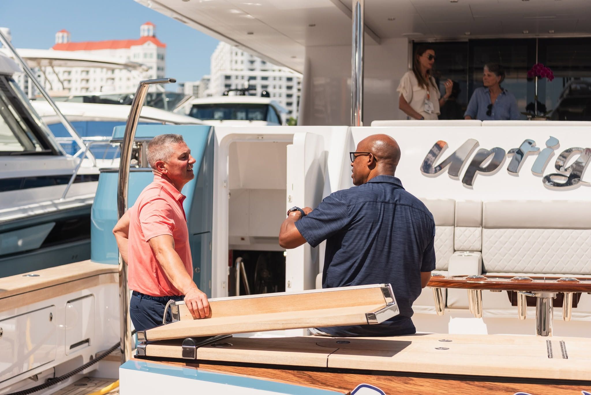 Two men on a luxury yacht discussing boat outfitting, one holds a wooden component.