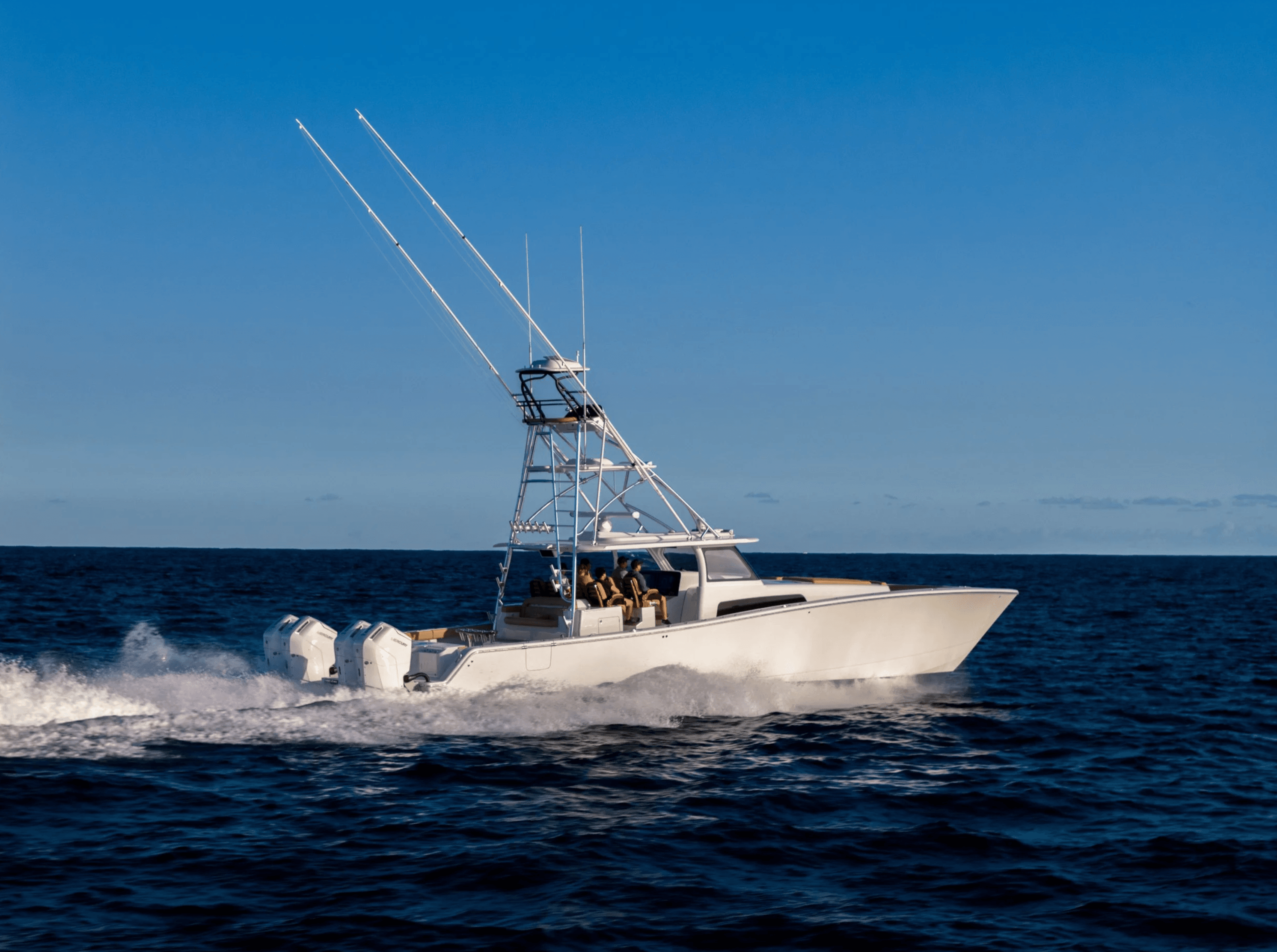 White fishing boat with outriggers speeding across clear blue ocean under a bright sky.