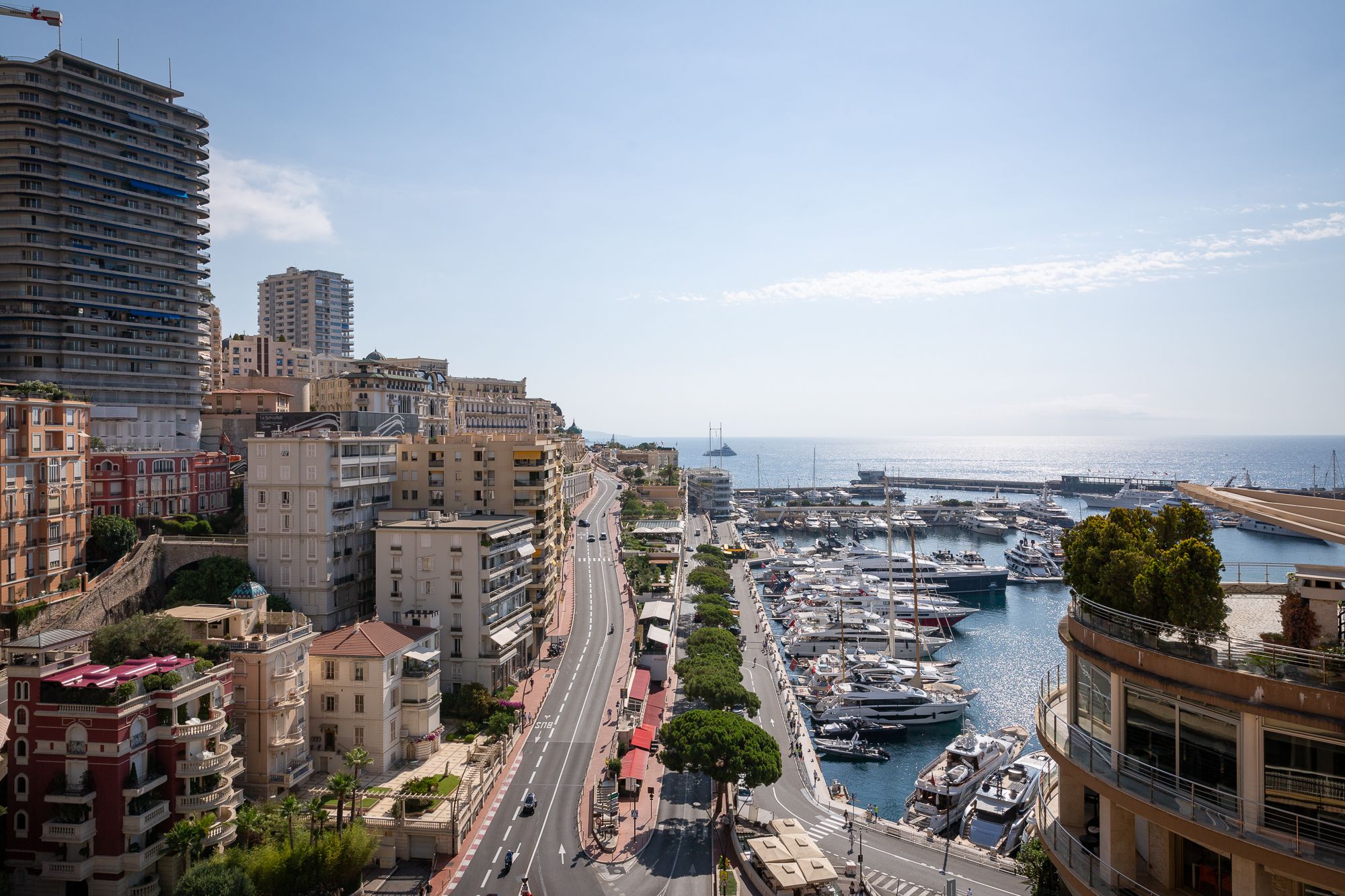 Monaco cityscape with tall buildings, a road, and a bustling marina filled with yachts.