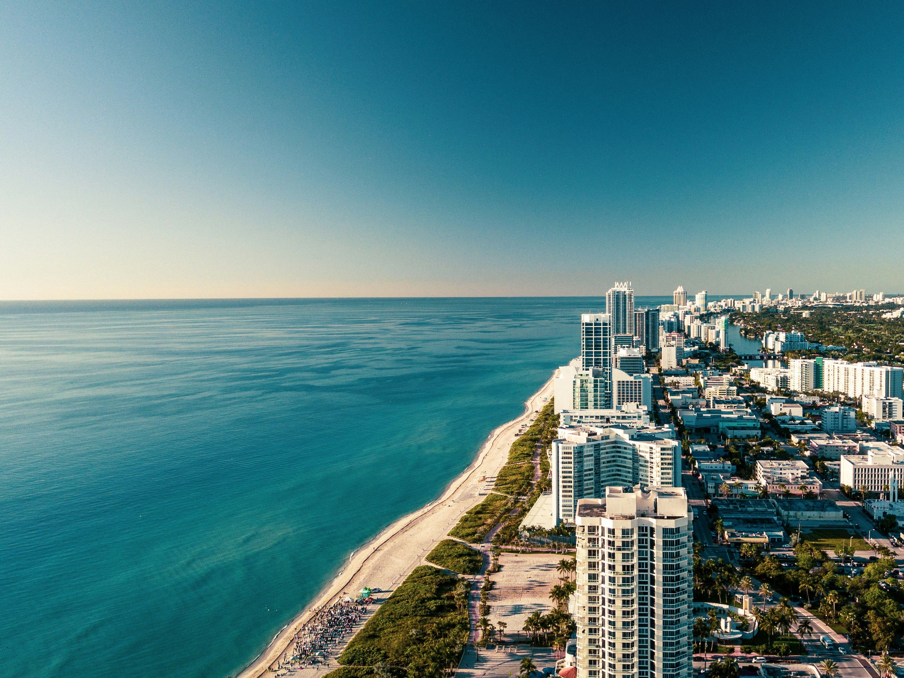 Aerial view of a vibrant coastal city with blue ocean, sandy beach, and tall buildings.