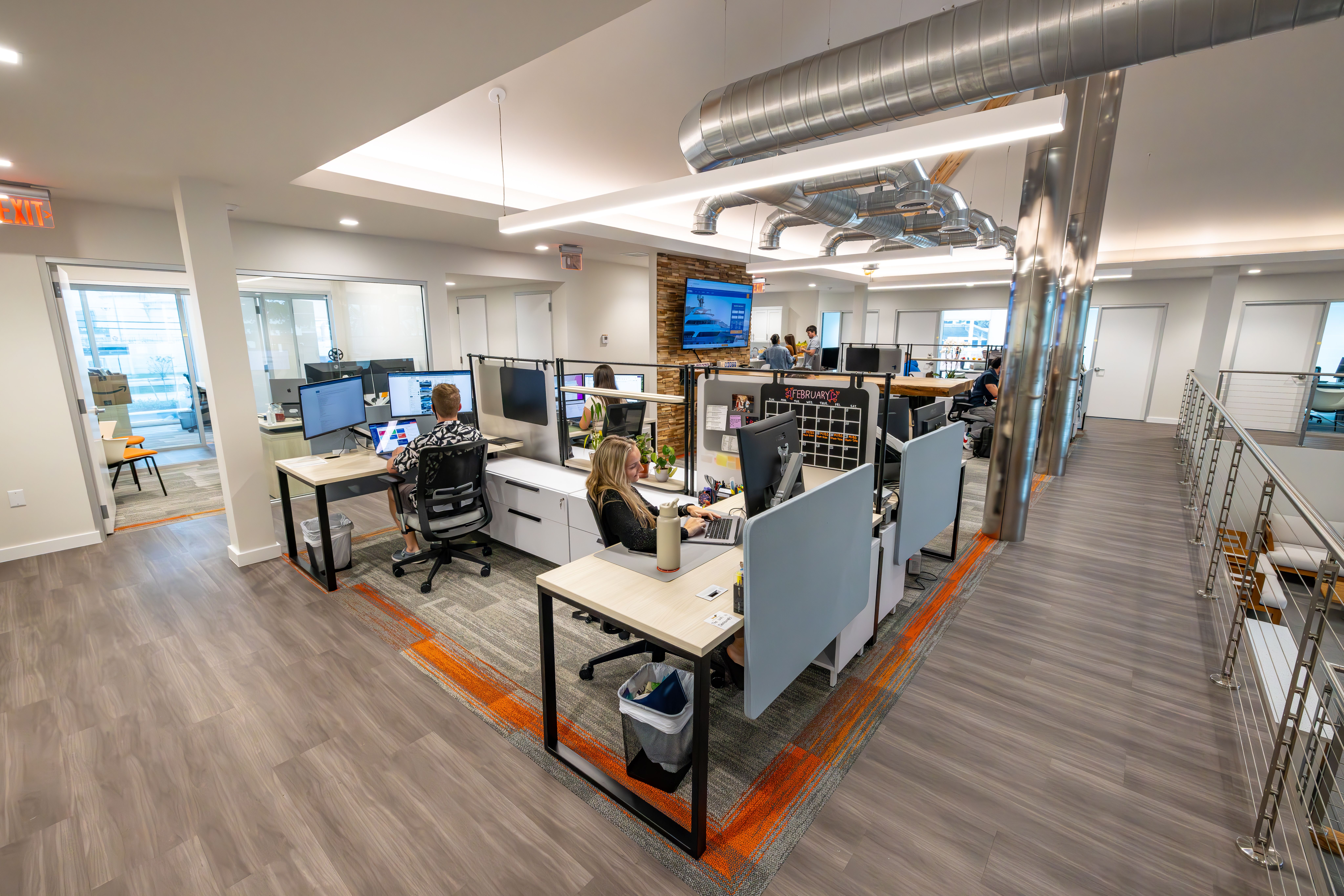 Modern open-plan office with employees working at multiple computer workstations.