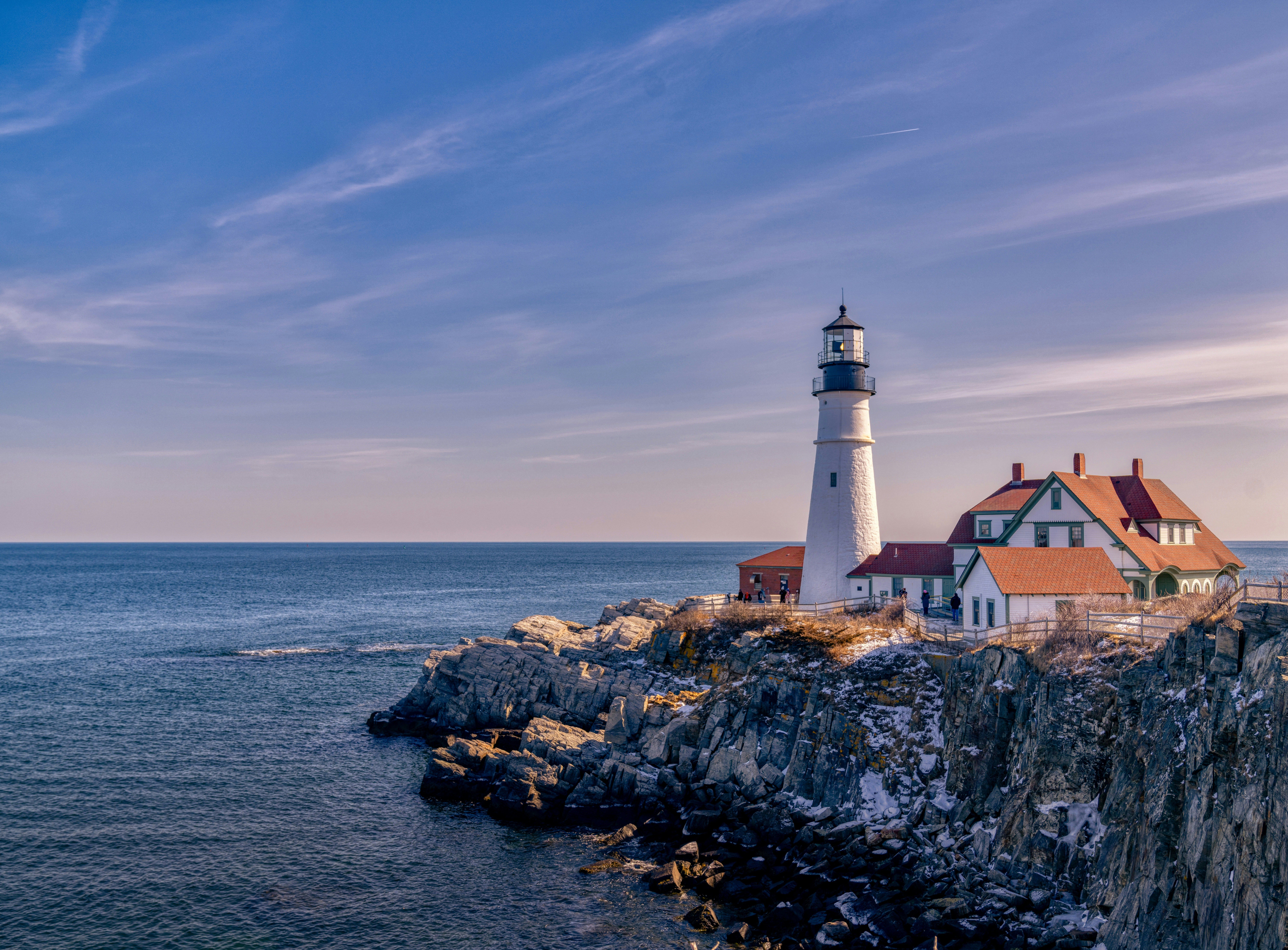 Historic white lighthouse on a rocky coast next to the vast blue ocean.