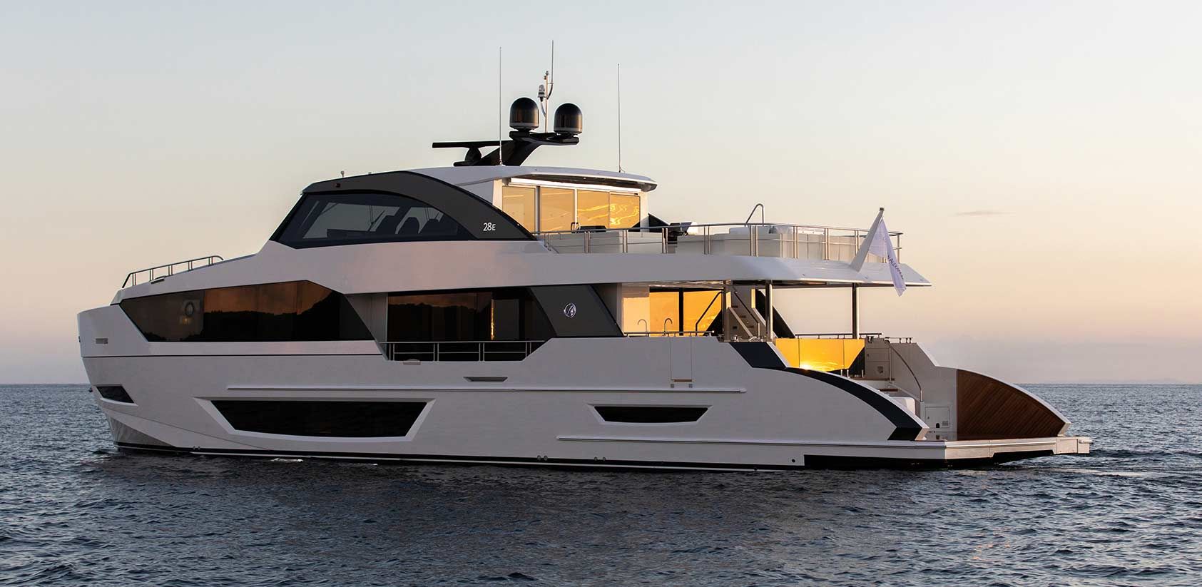 Sleek white luxury yacht with illuminated windows cruises on calm water at golden hour.