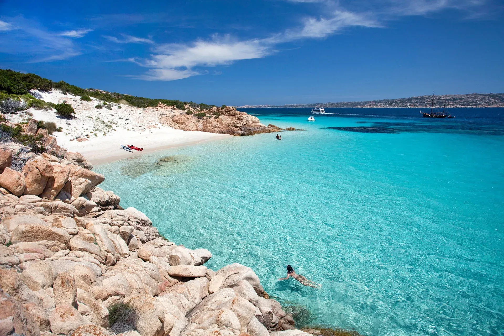 Crystal clear turquoise water laps against a white sand beach and rocky shore.