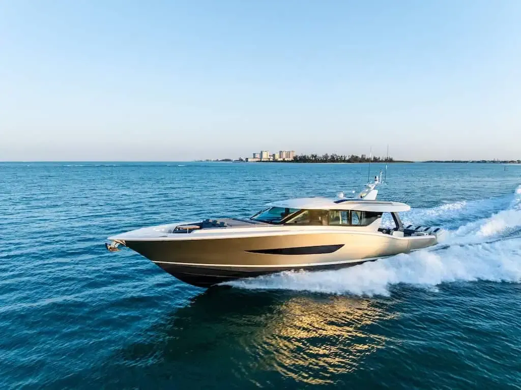 Golden luxury yacht speeding across blue water, creating a wake, with a distant city.