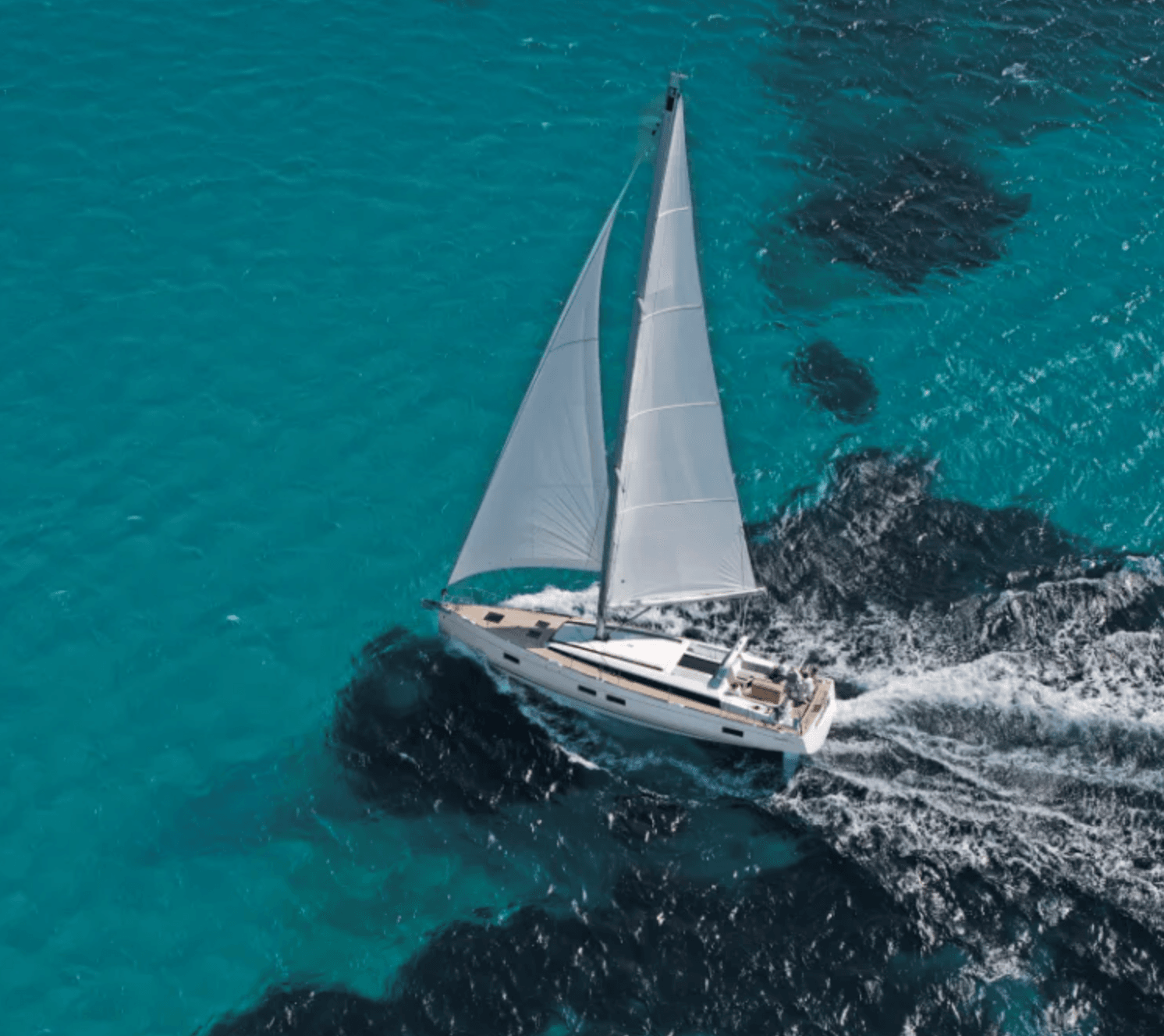 White sailboat with full sails glides across clear turquoise water, leaving a wake.
