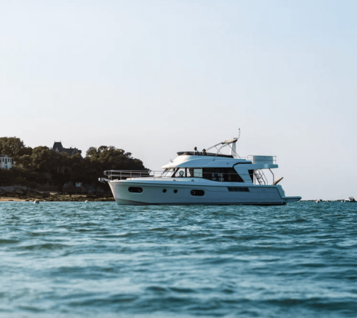 White yacht on blue water with a tree-lined coast in the background.