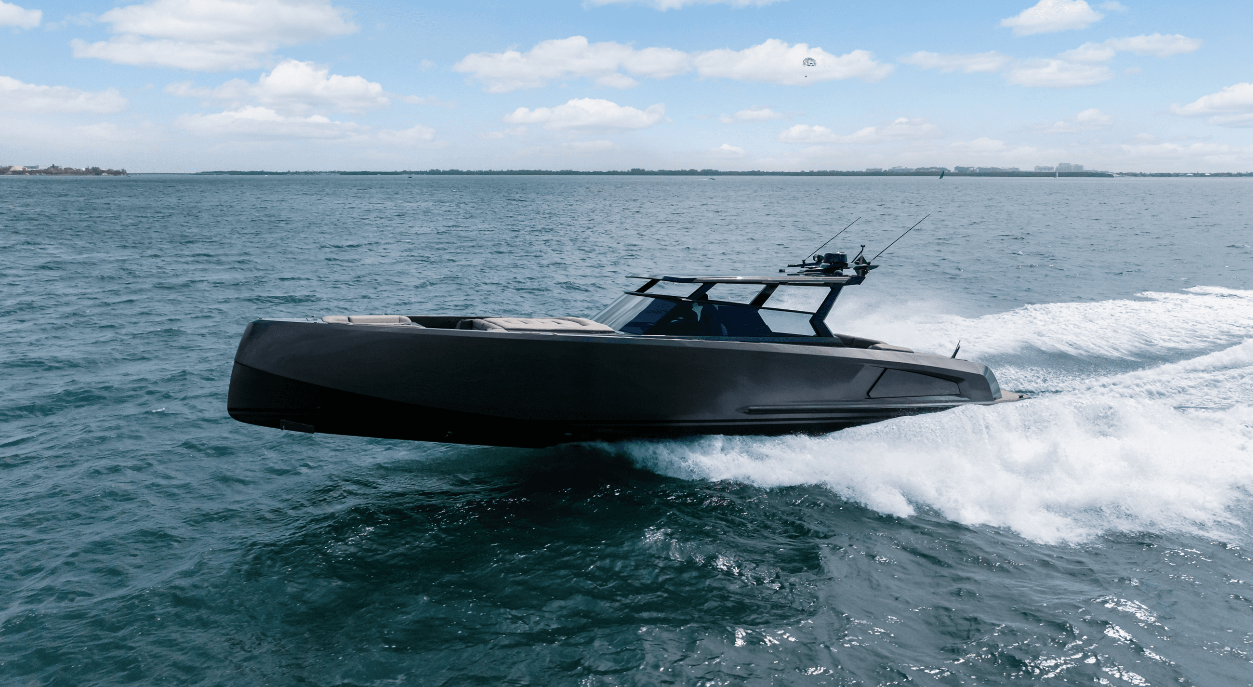 A sleek dark motor yacht glides across blue water, creating a white wake.