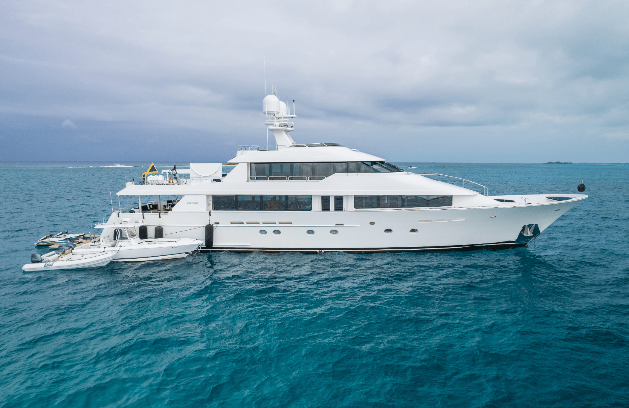 Large white luxury yacht with tenders in clear blue ocean water under a cloudy sky.