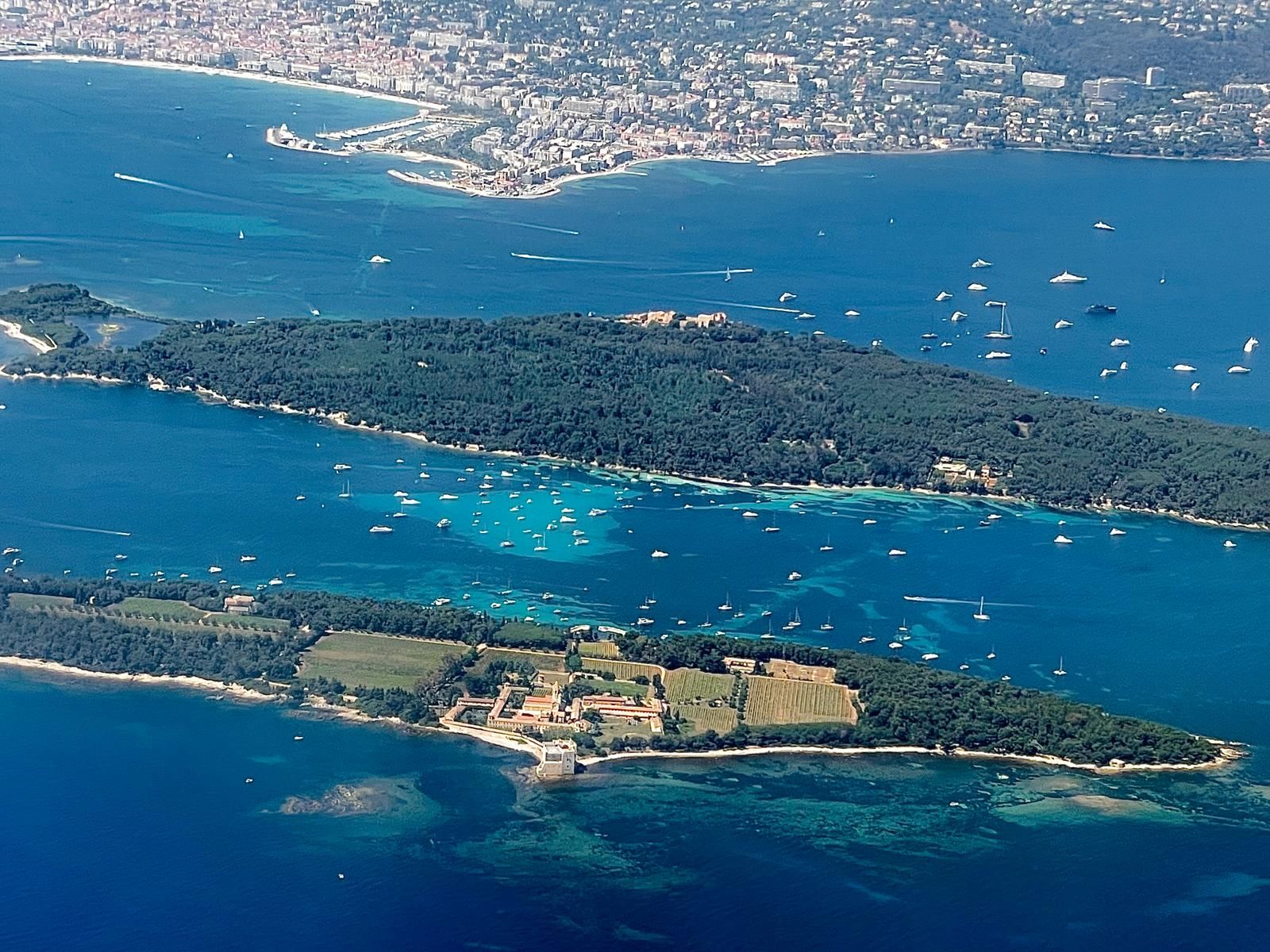 Aerial view of two green, forested islands in a blue sea with numerous boats.