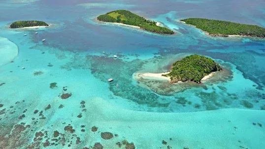 Aerial view of lush green islands surrounded by clear turquoise ocean water and coral reefs.