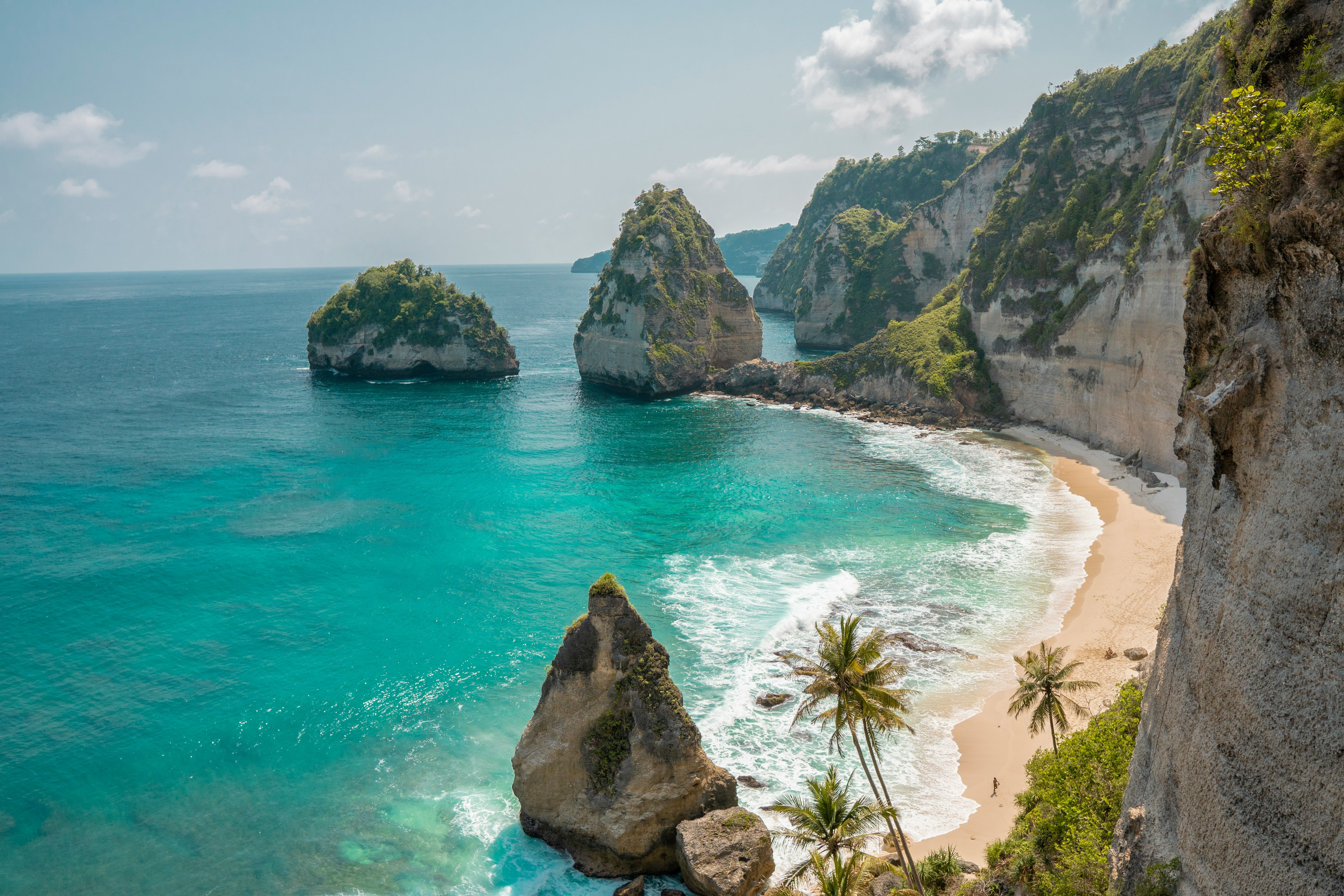 Tropical bay with turquoise water, sandy beach, rocky islets, and lush cliffs.