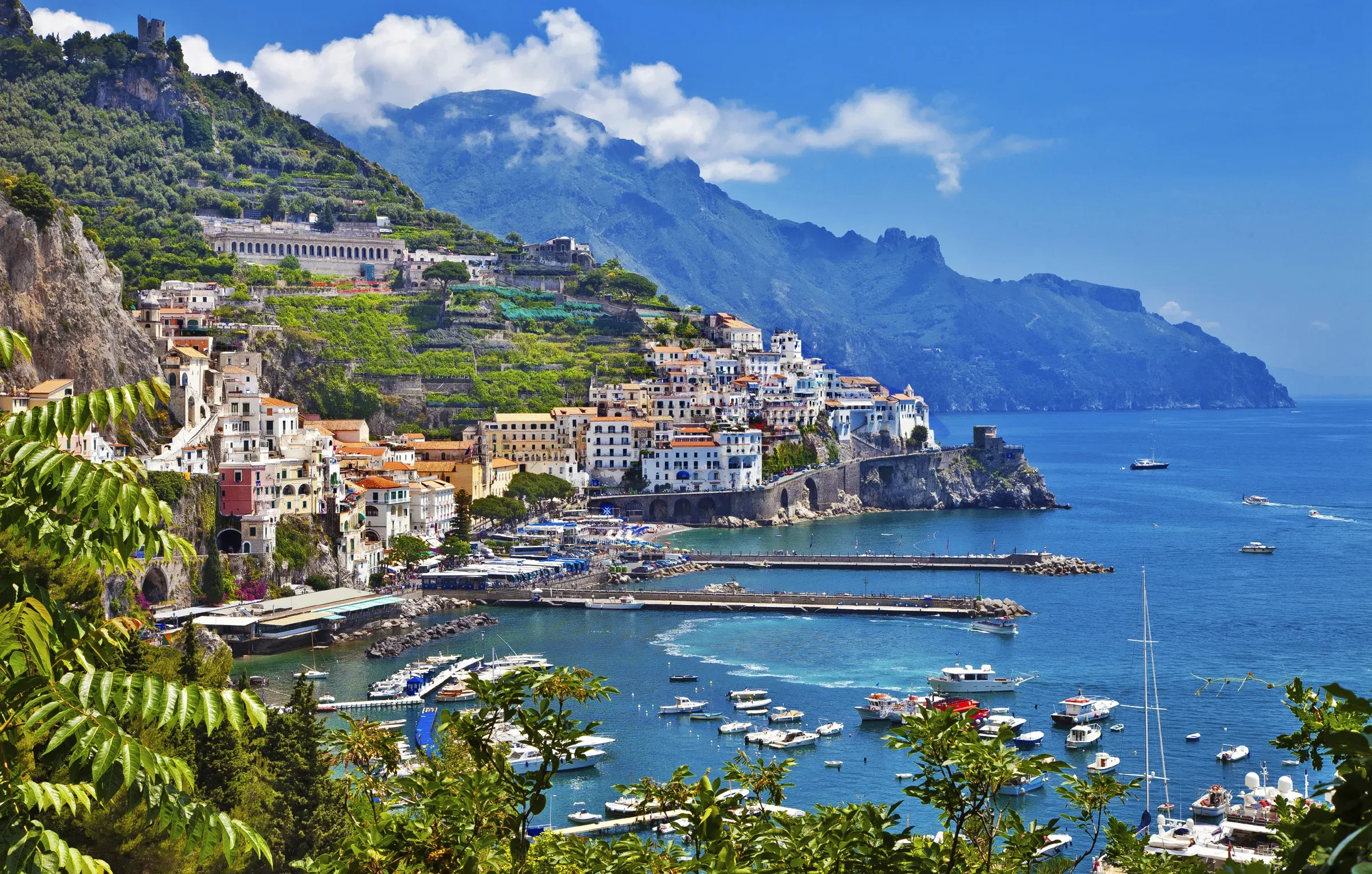 Colorful coastal town nestled on a hillside overlooking a bay filled with boats.