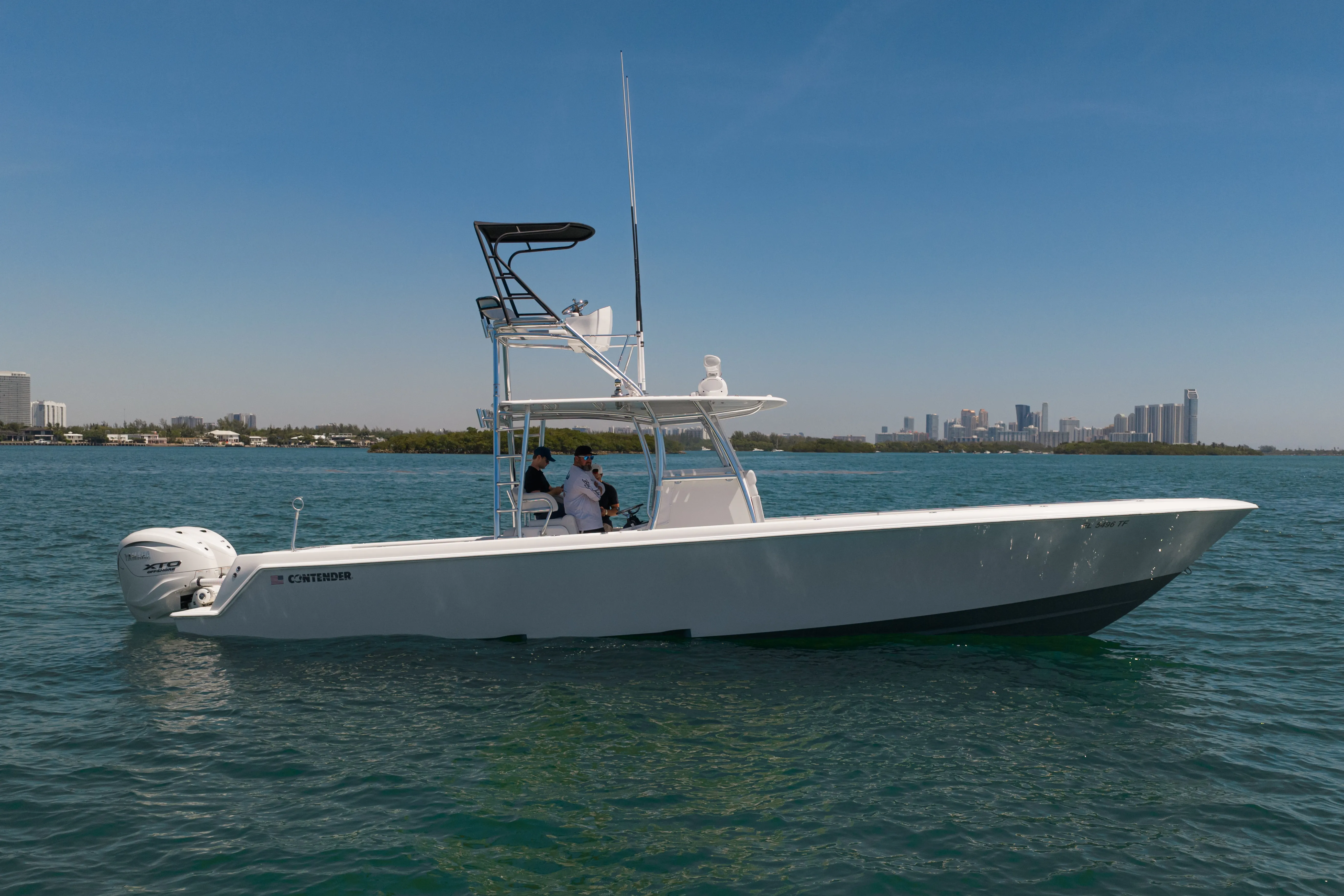 White center console boat with two people navigating calm blue water near a city skyline.