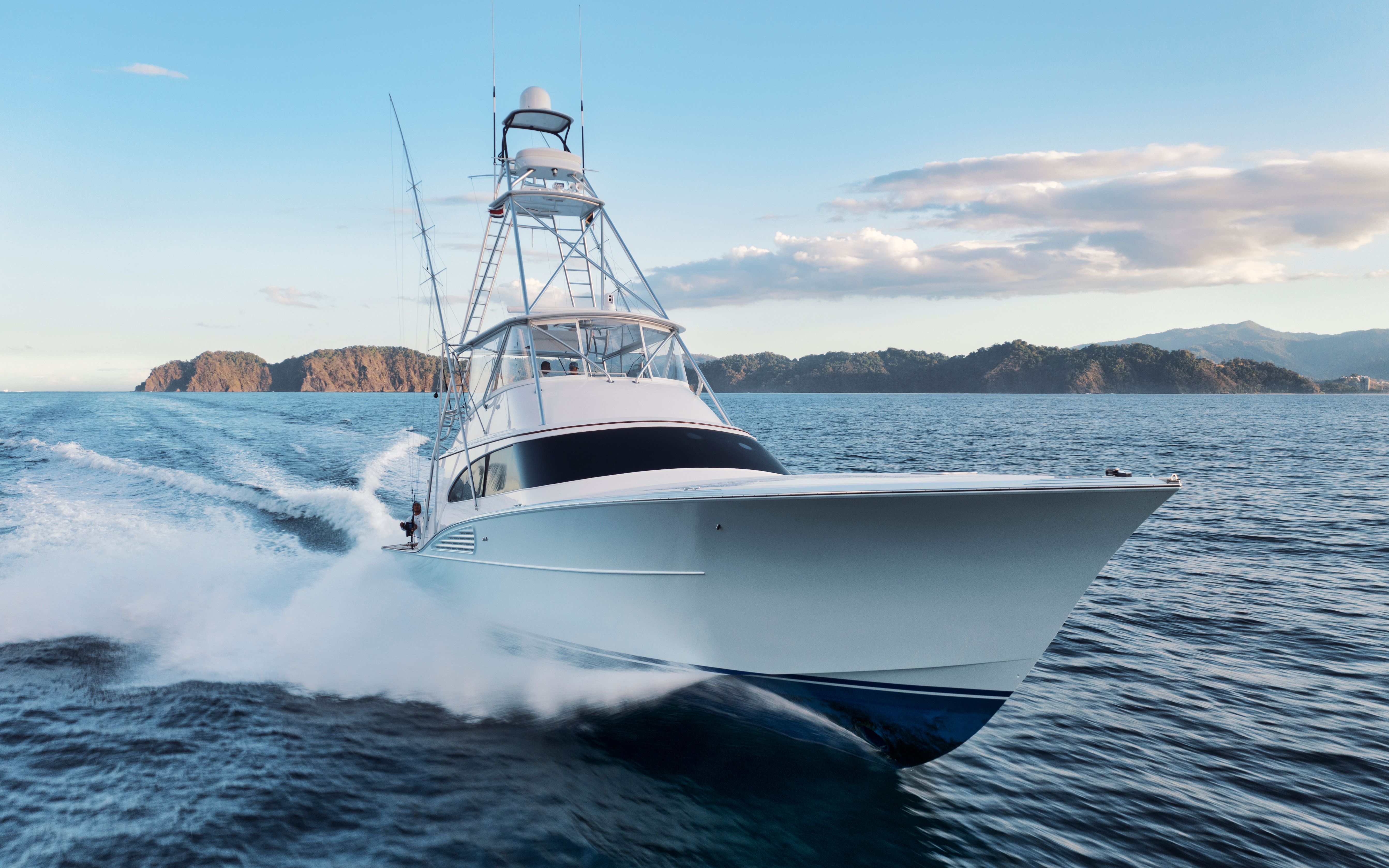 A large white fishing boat speeds across blue water with mountains in the background.