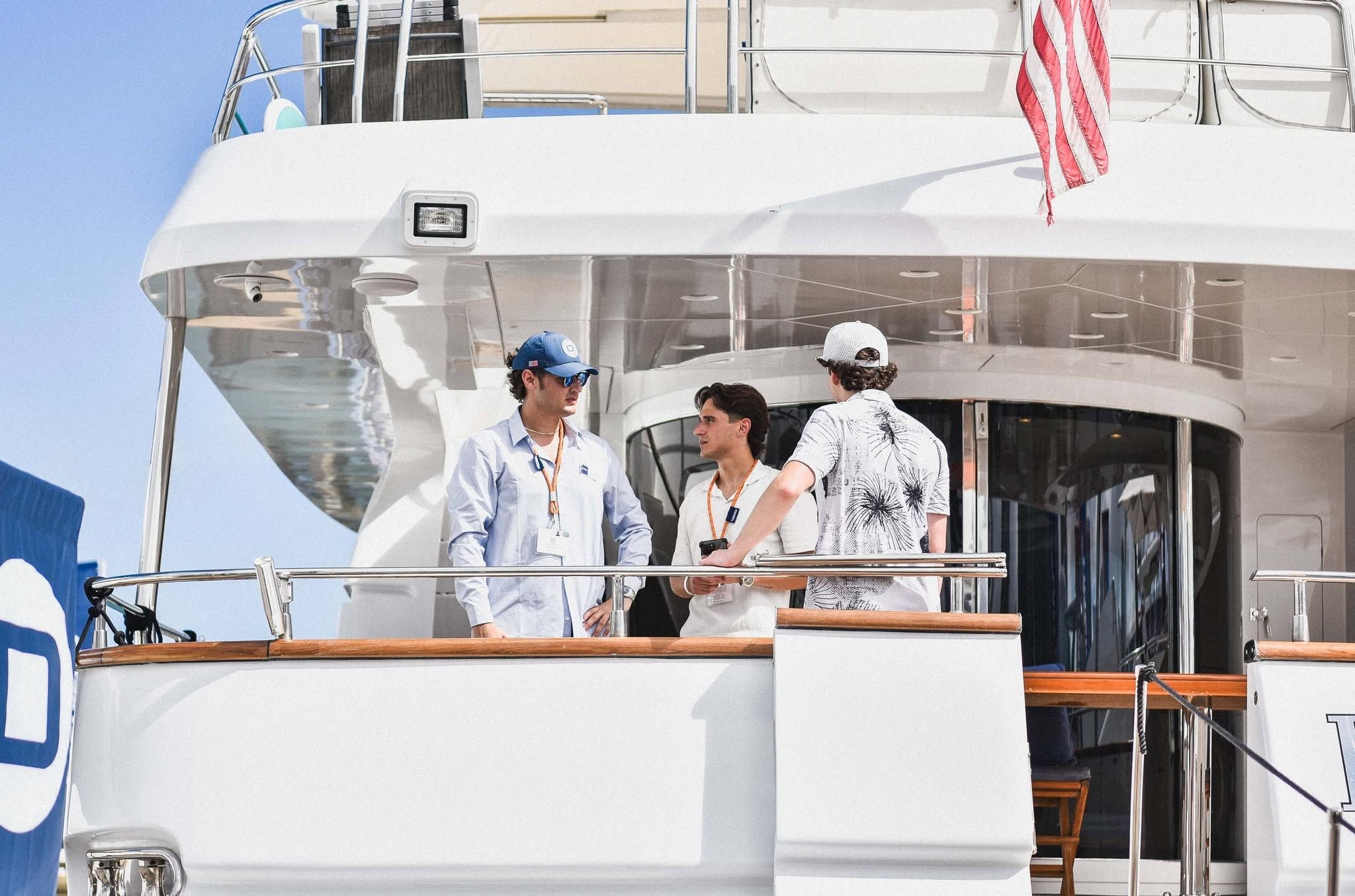 Three men in casual attire chatting on the stern deck of a large white yacht.
