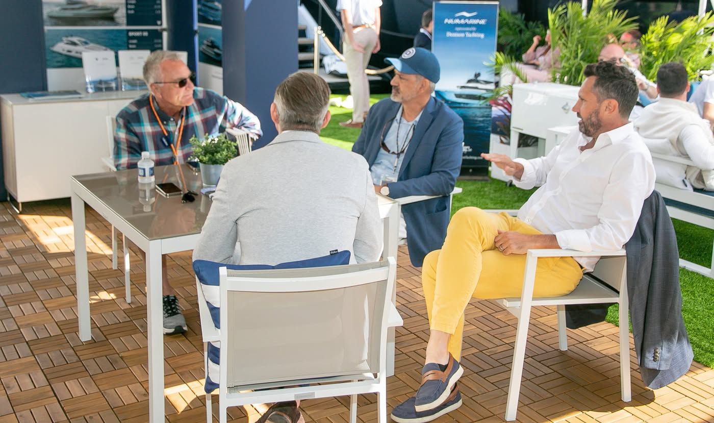 Four men are seated at an outdoor table, actively conversing during a sunny event.