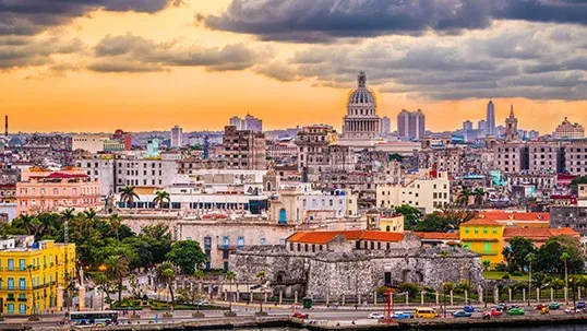 Havana cityscape at sunset with El Capitolio dome, historic buildings, and waterfront.
