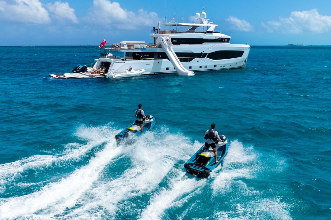 Two people on jet skis creating wakes near a large white yacht with a slide.