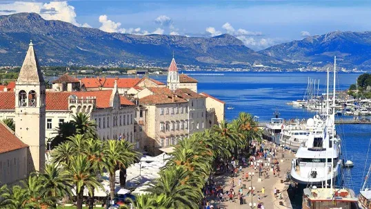 Beautiful Croatian coastal town featuring historic architecture, bustling promenade, marina, and mountains.