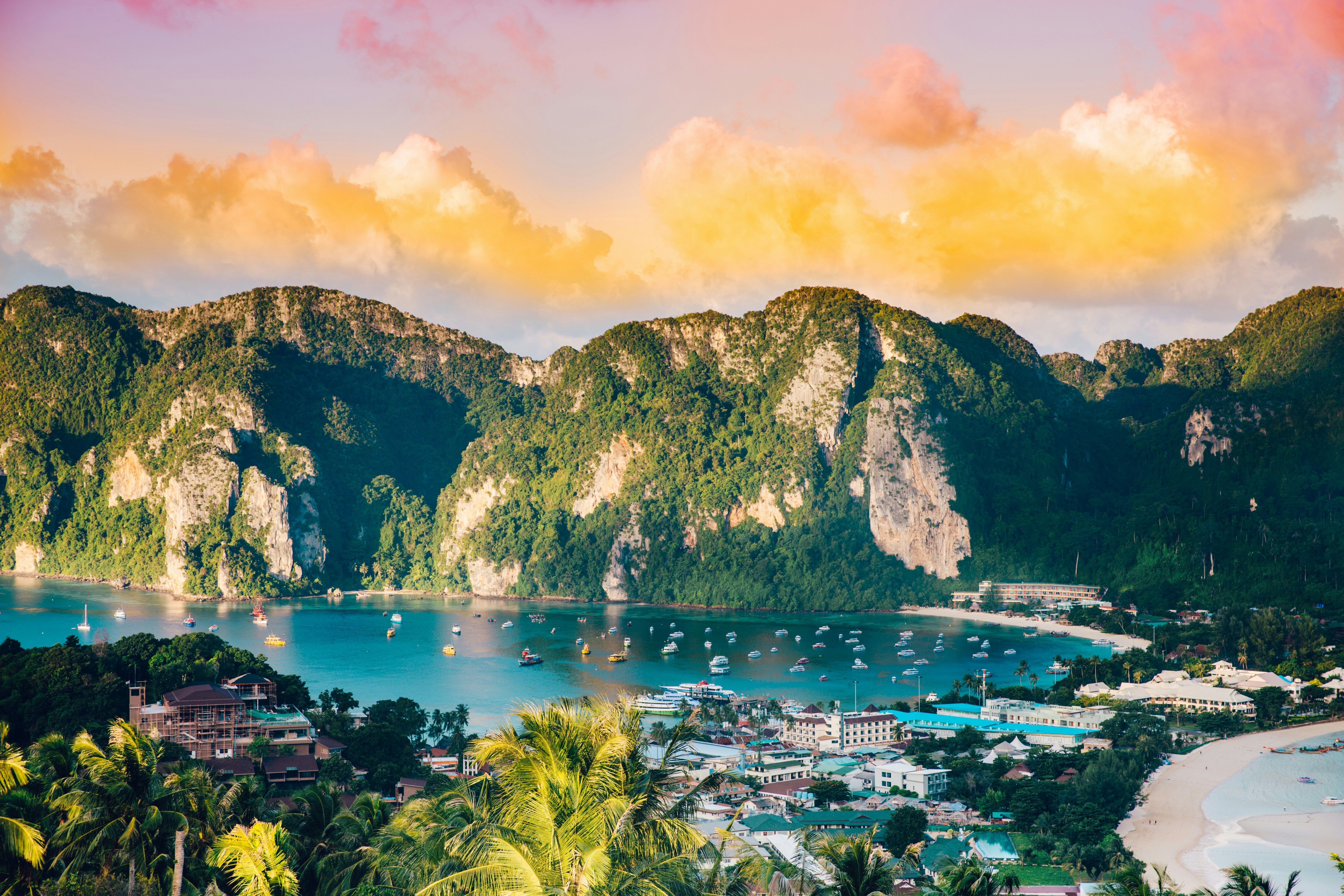 Vibrant sunset over a tropical bay with boats, lush green islands, and a coastal town.