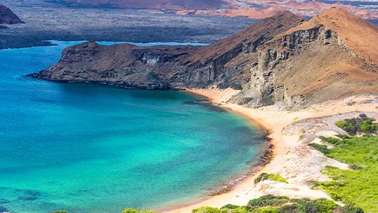 Turquoise bay with a sandy beach, rugged volcanic cliffs, and sparse green vegetation.