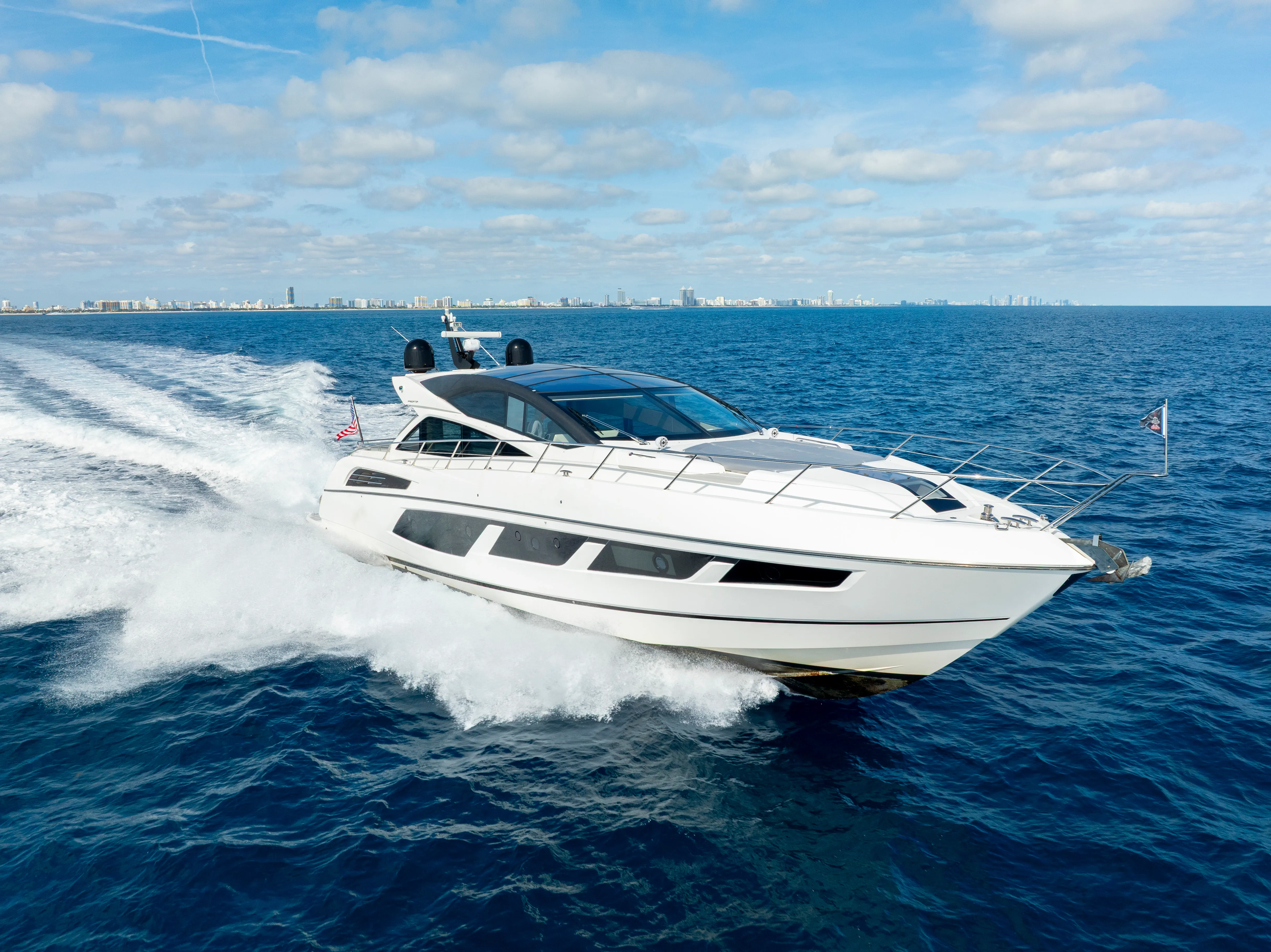 White luxury yacht speeds across deep blue water, leaving a prominent white wake.