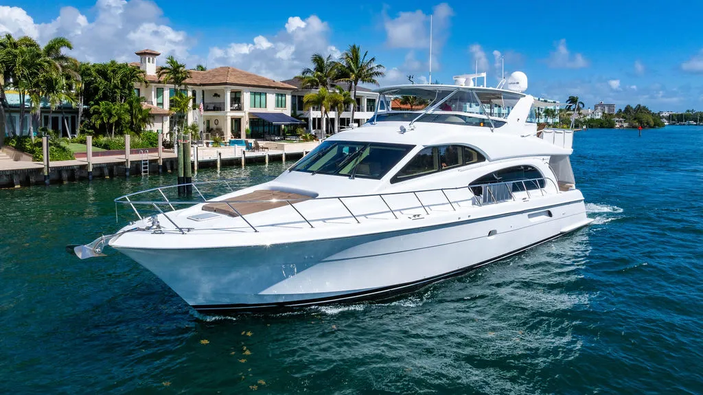A large white motor yacht cruises on blue water past luxurious waterfront homes.