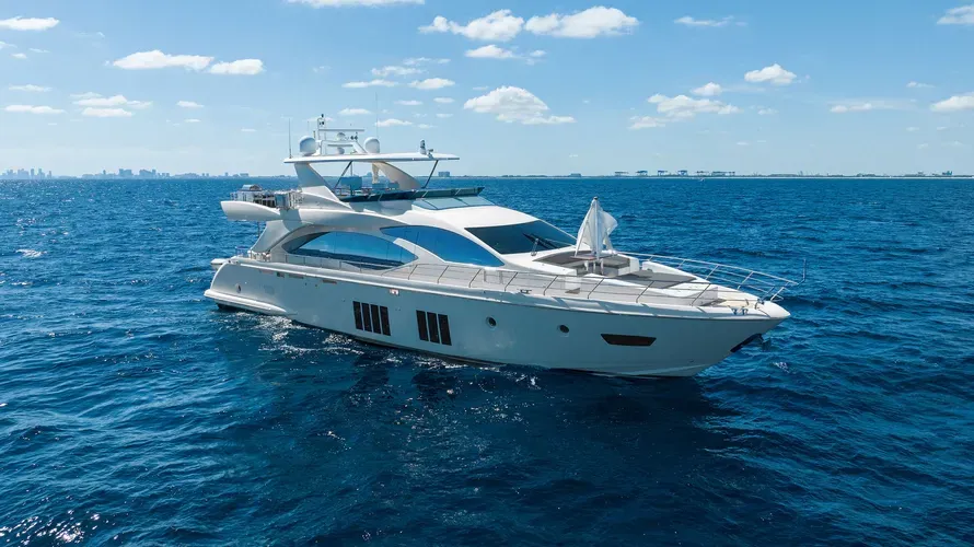 A large white luxury yacht cruises on clear blue ocean waters under a sunny sky.