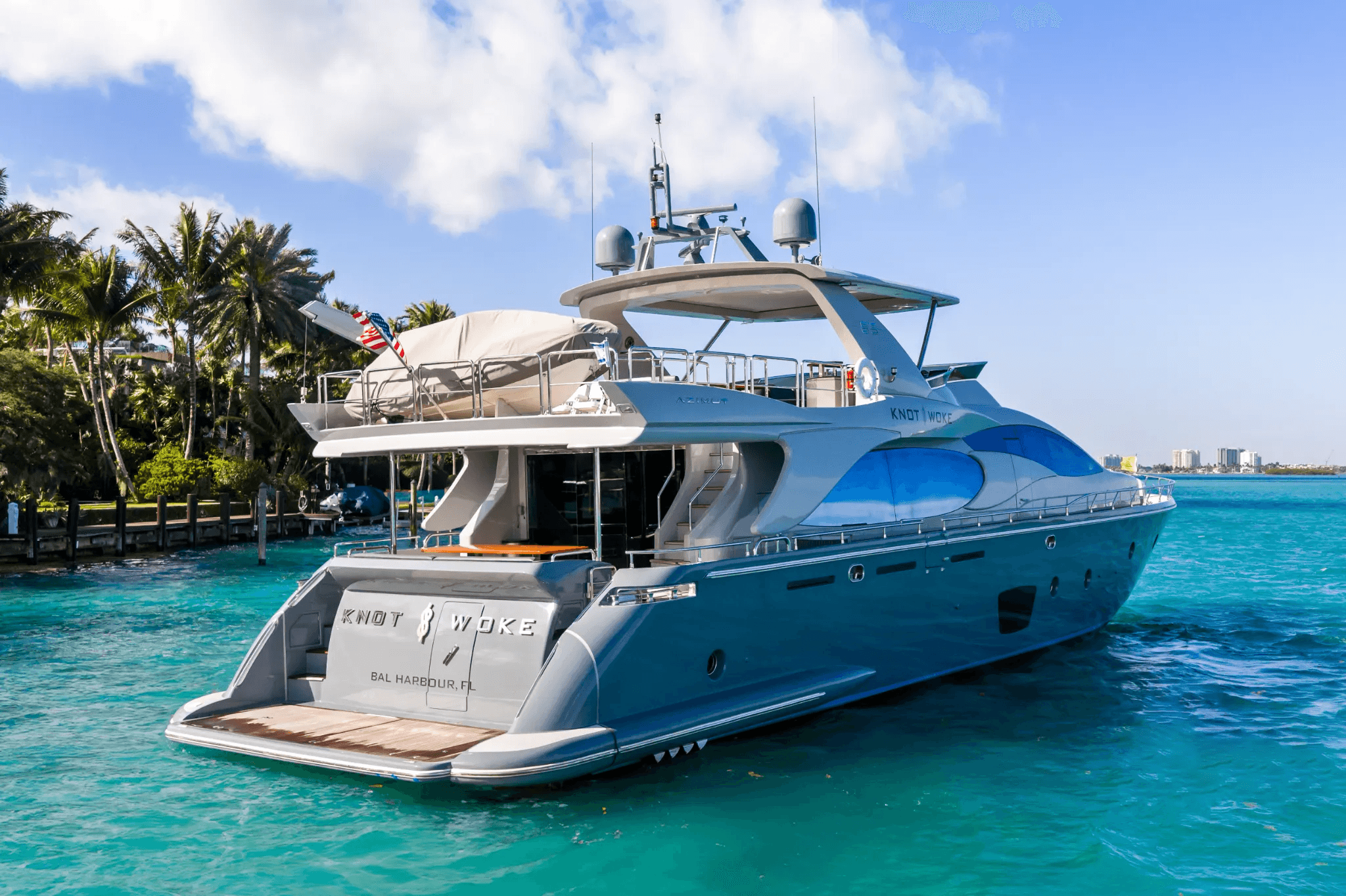 Stern view of a luxurious grey motor yacht with blue windows docked in turquoise water.