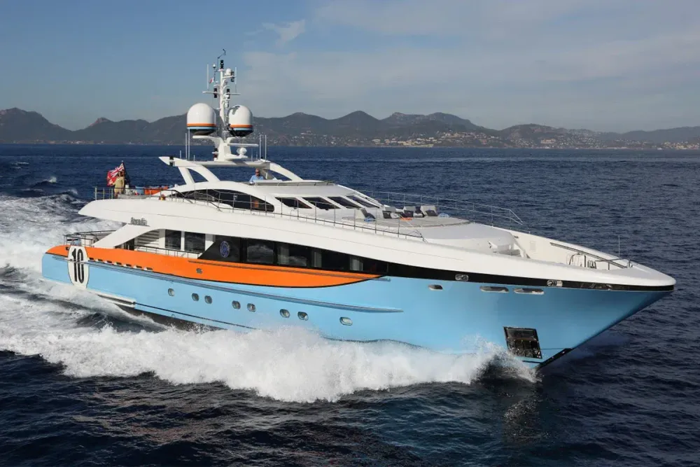 A large light blue and orange luxury yacht cruises through deep blue water.