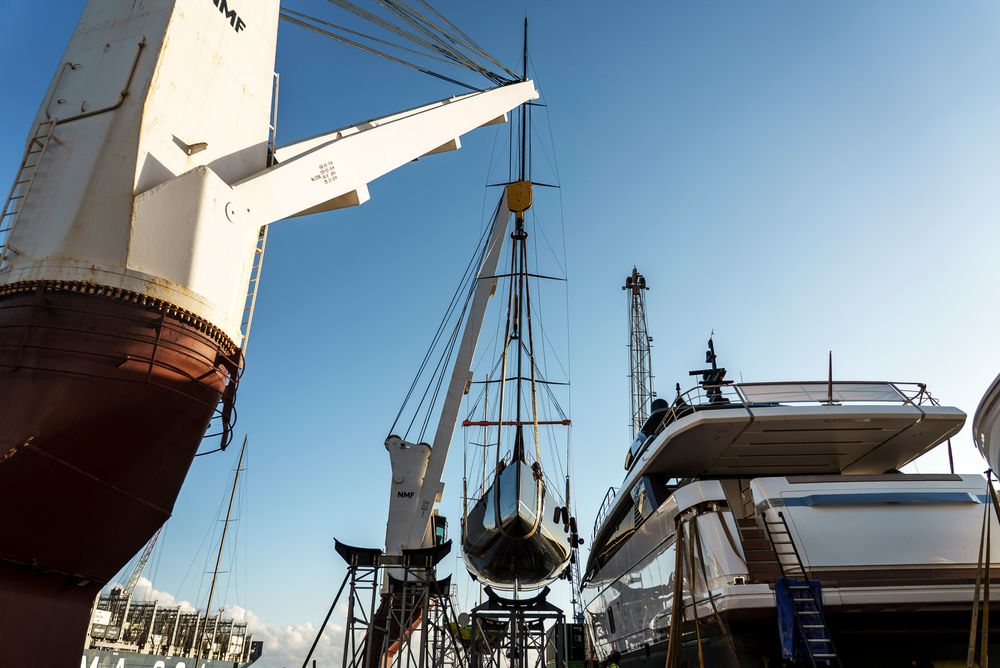 A large ship's crane lifts a small yacht, alongside another luxury vessel on deck.