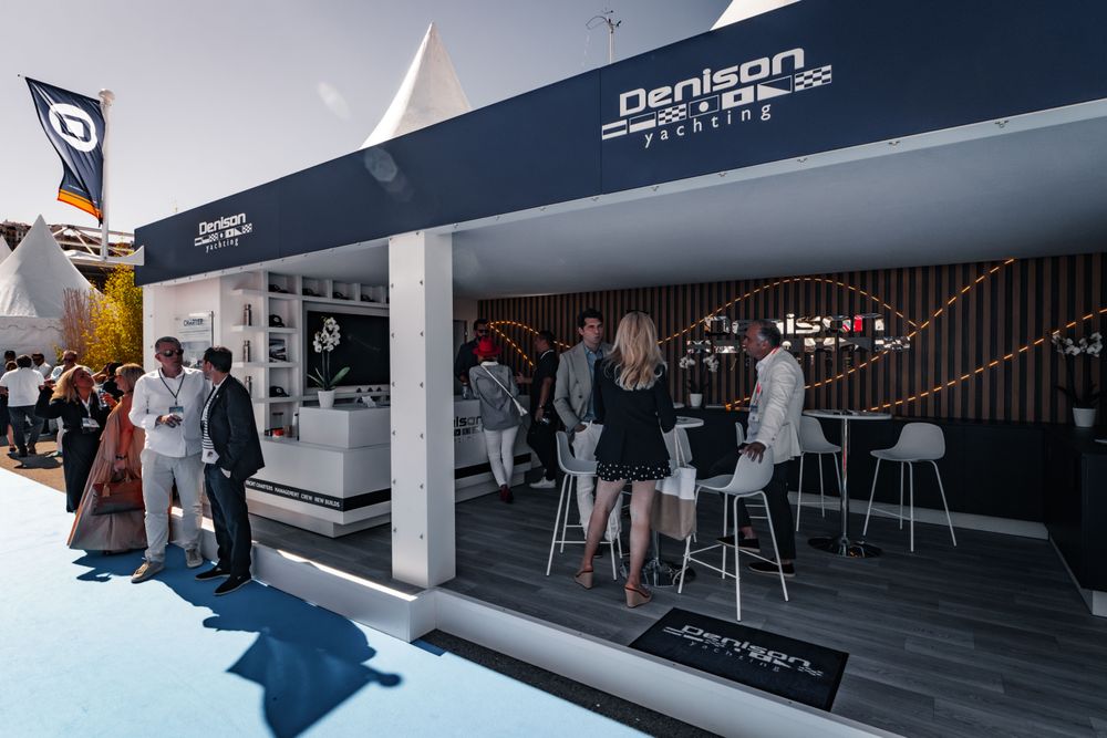 People socialize inside and outside the Denison Yachting booth at an outdoor event.