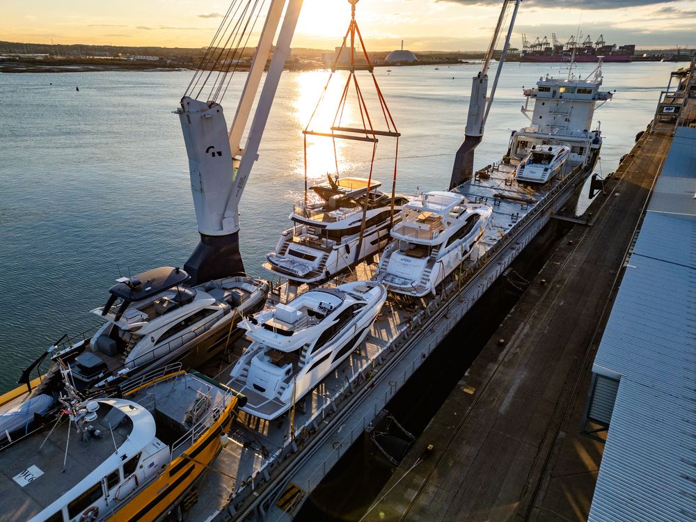 Cargo ship loaded with luxury yachts at sunset, a crane preparing to move one.